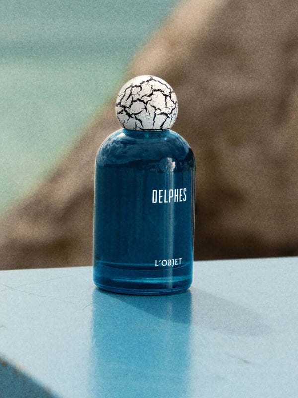 Blue perfume bottle with a cracked white cap on a reflective surface